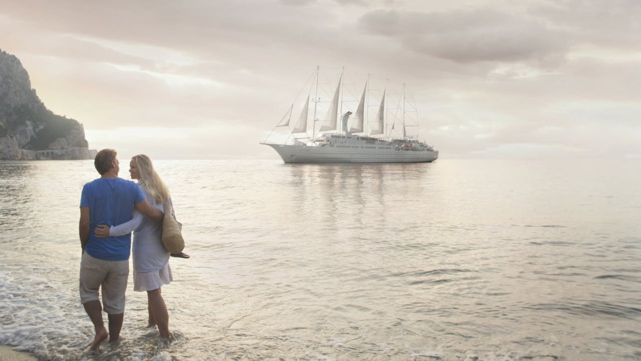 Couple walking the beach with Windstar yacht behind them