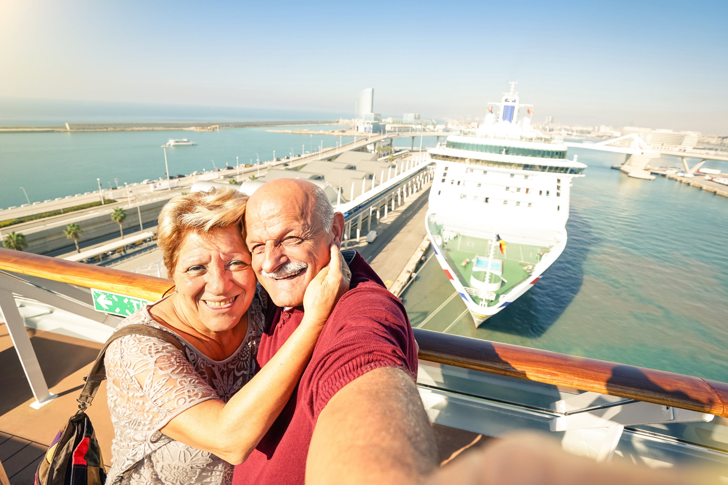 Senior couple taking selfie in front of cruise ship.